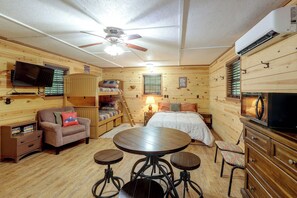 Una habitación acogedora de estilo cabaña con una cama, un escritorio, una silla, un televisor y un ventilador de techo.