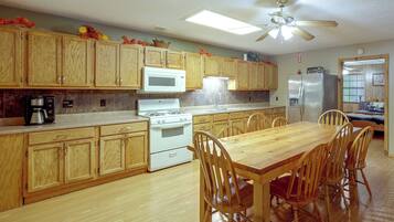 A kitchen with wooden cabinets, a stove, a microwave, a refrigerator, and a dining table with chairs.