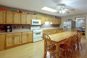 A kitchen with wooden cabinets, a stove, a microwave, a refrigerator, and a dining table with chairs. - Wolf Pen Gap Getaway in 3 Cabins, Sleeps 32! (Mena)