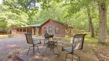 A cabin with a porch, a grill, and two chairs.