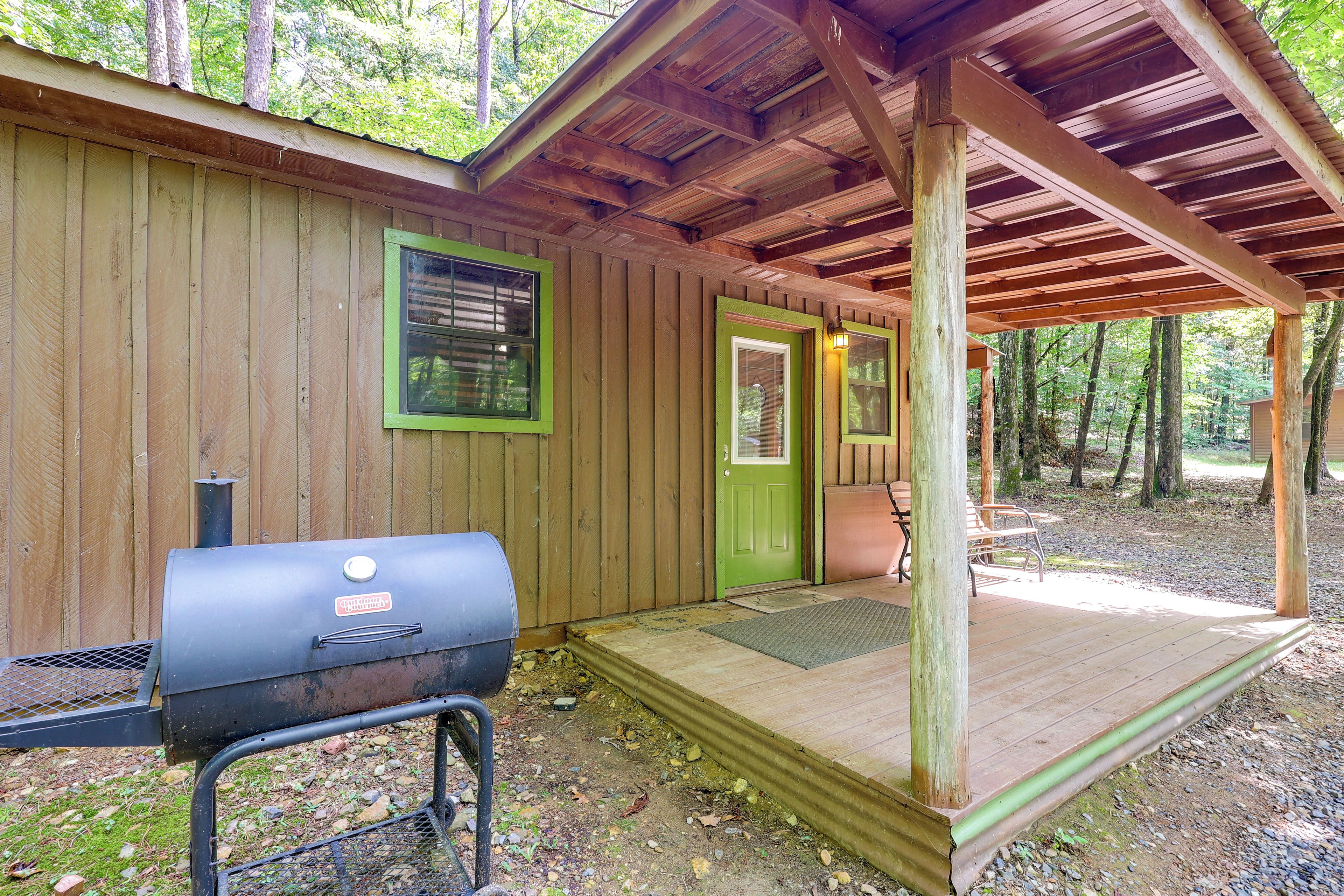 A wooden cabin with a porch, a grill, and a door with a window.