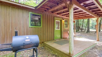 A wooden cabin with a porch, a grill, and a door with a window.