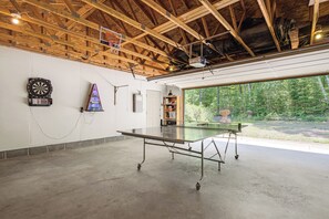 A spacious indoor area with a ping pong table, dartboard, and a small shelf with items. - Gilmore Lake Family Escape w/ Game Room & Dock! (Minong)