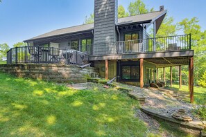 A modern two-story house with a balcony, a covered outdoor seating area, and a stone retaining wall. - Gilmore Lake Family Escape w/ Game Room & Dock! (Minong)