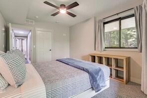 A bedroom with a bed, a ceiling fan, a window with curtains, and a door leading to another room.