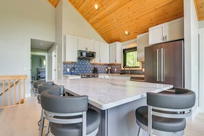 A modern kitchen with a large island, white cabinets, and a stainless steel refrigerator.