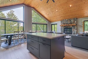 A spacious kitchen with a large island, a stone fireplace, and large windows offering views of the outdoors.