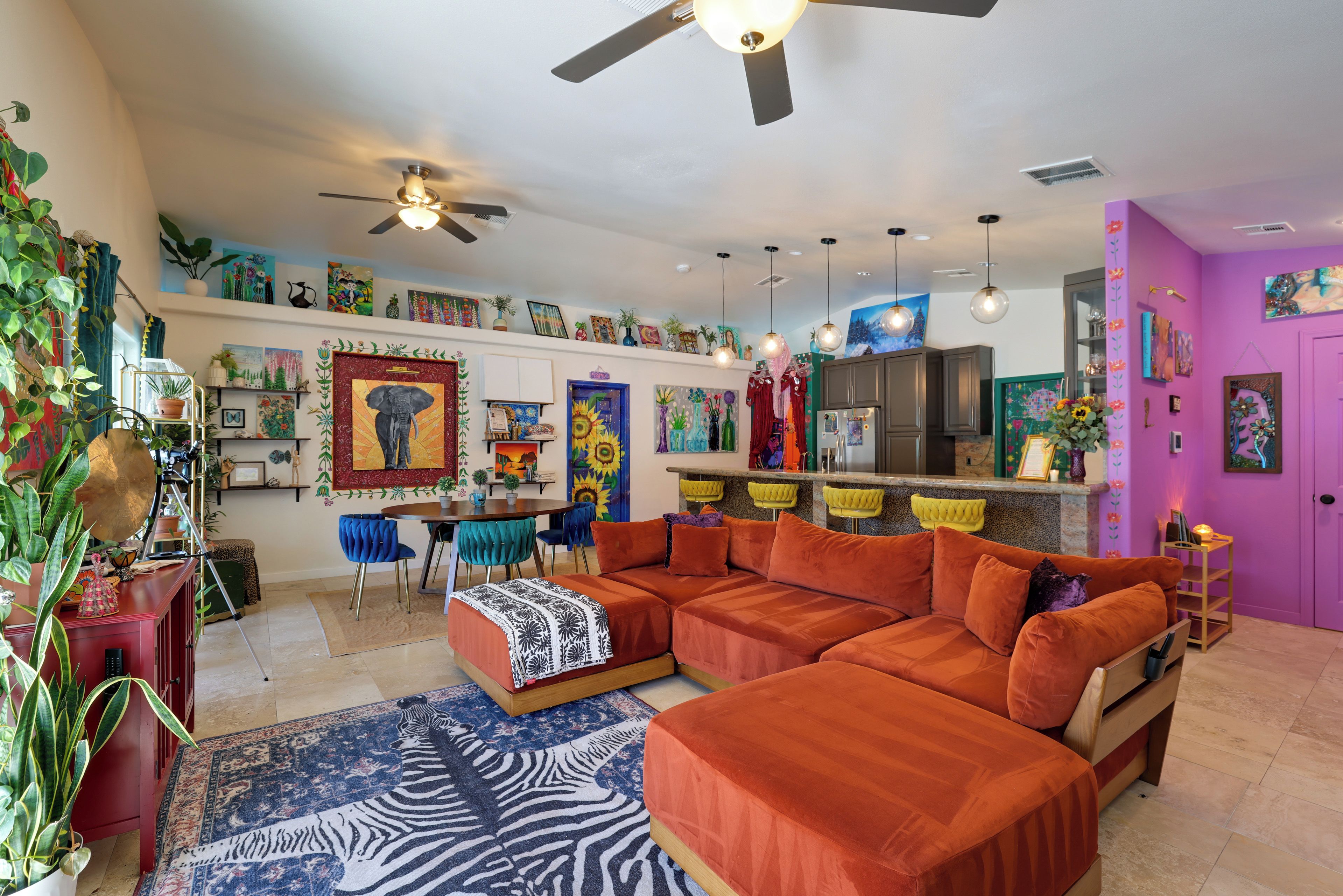 A modern living room with a sectional sofa, a zebra-patterned rug, and a variety of artwork on the walls.