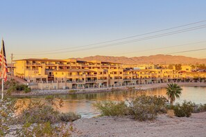 Ein mehrstöckiges Hotel mit Balkonen, ein Fluss im Vordergrund und Berge im Hintergrund.