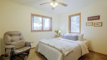 A bedroom with a bed, a recliner, two windows, a ceiling fan, and a wall-mounted sign.