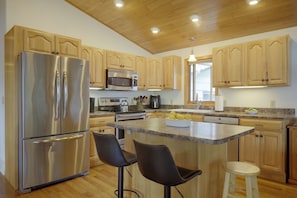 A modern kitchen with wooden cabinets, stainless steel appliances, and a central island with seating. - Lakefront Crystal Falls Home w/ Private Dock (Crystal Falls)
