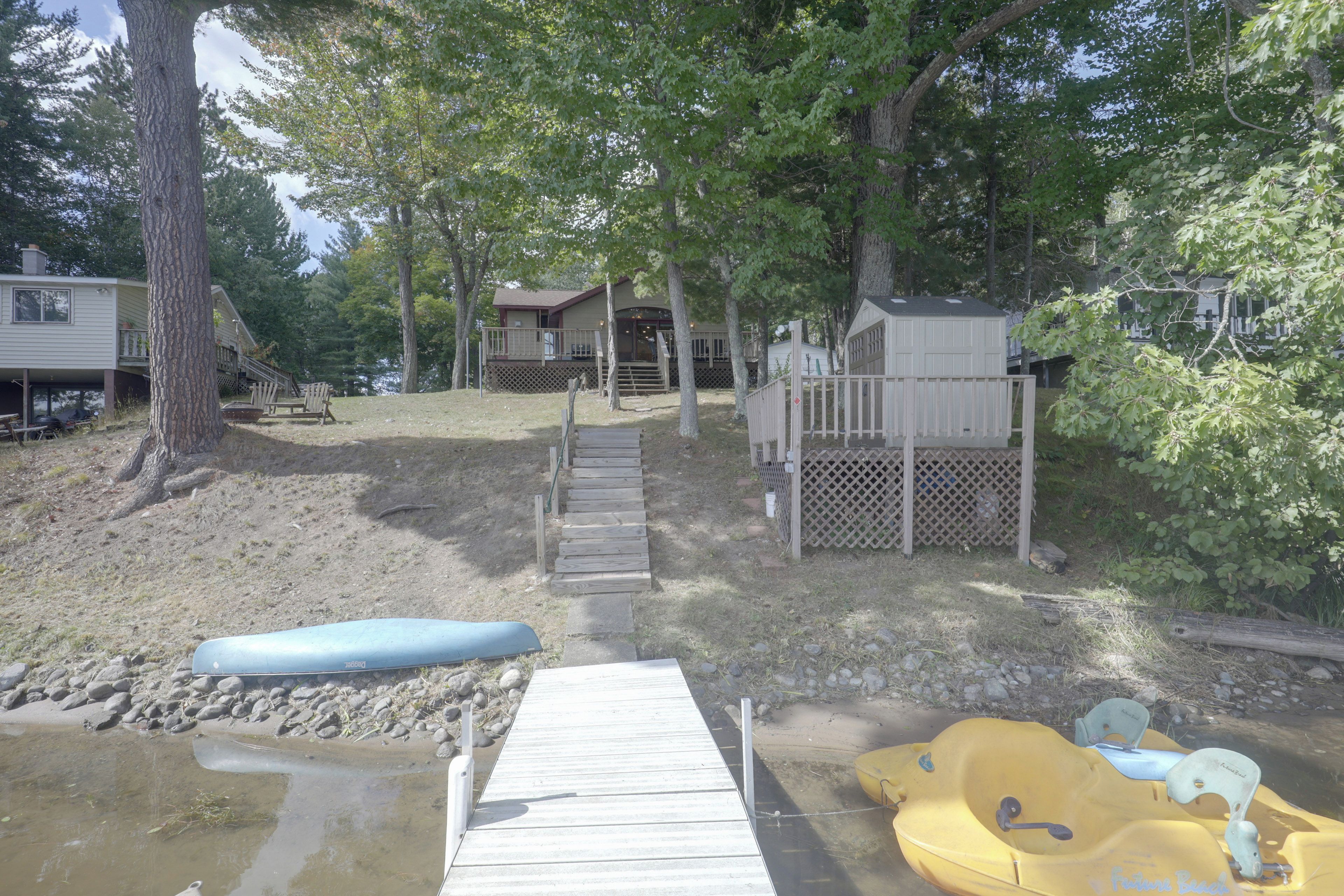 A wooden dock leading to a sandy beach area with a kayak and a paddleboard.