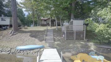 A wooden dock leading to a sandy beach area with a kayak and a paddleboard.