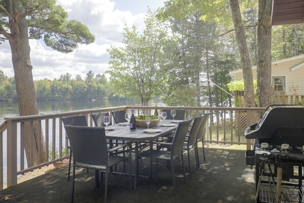 An outdoor dining area with a table set for two, surrounded by chairs, overlooking a body of water with trees in the background. - Lakefront Crystal Falls Home w/ Private Dock (Crystal Falls)