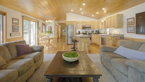 A spacious living room with a wooden coffee table, two sofas, and a kitchen in the background. - Lakefront Crystal Falls Home w/ Private Dock (Crystal Falls)