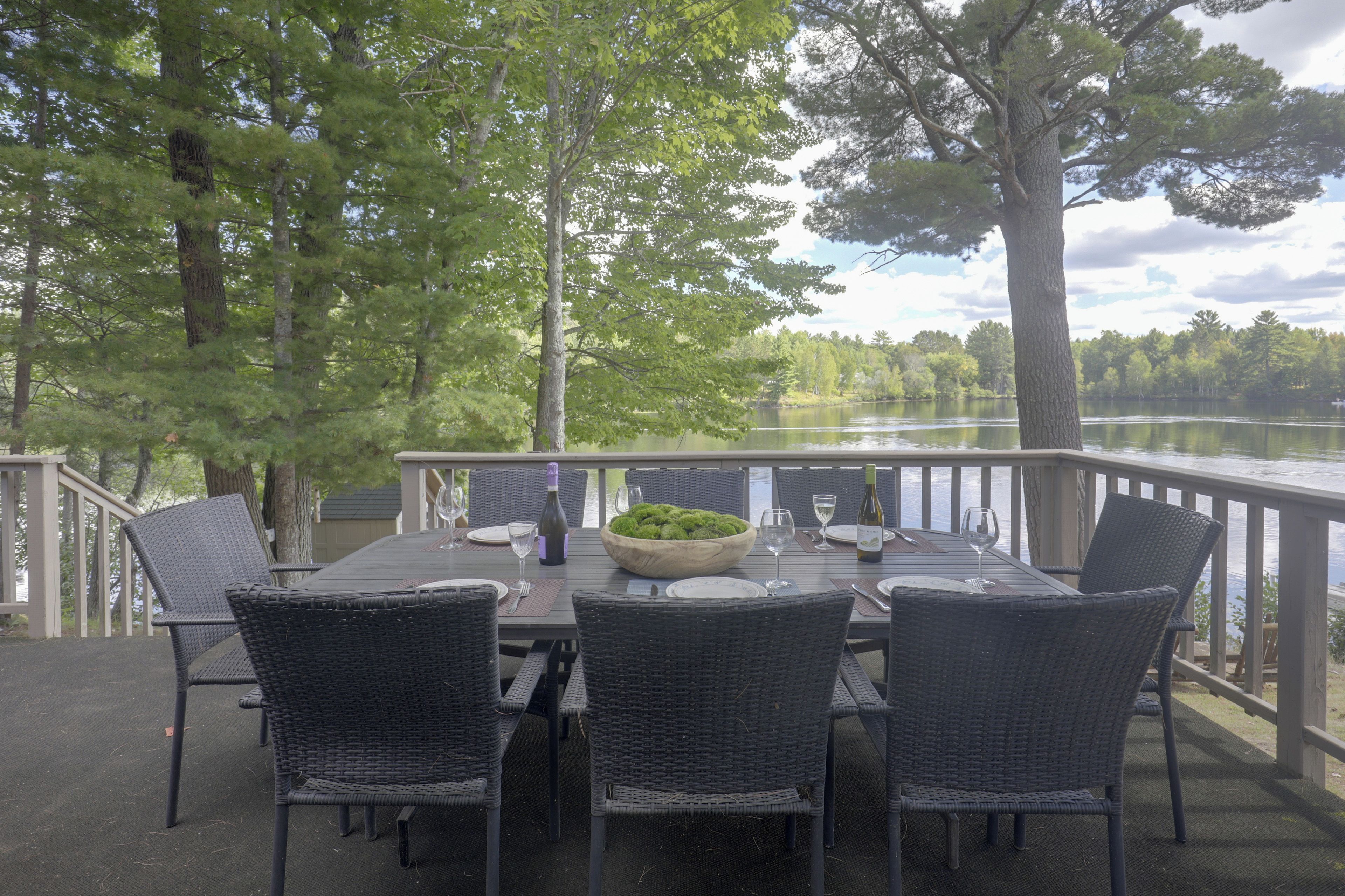 An outdoor dining area with a table set for four, surrounded by chairs, overlooking a lake.