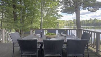An outdoor dining area with a table set for four, surrounded by chairs, overlooking a lake.