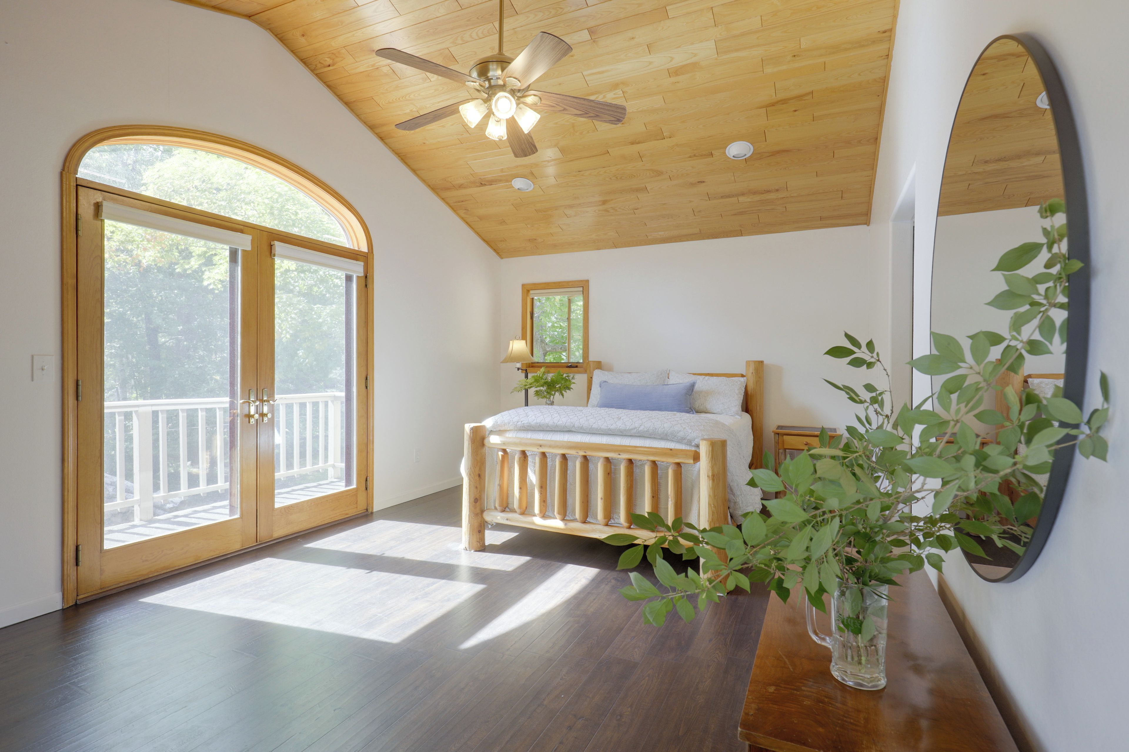 A bedroom with a wooden ceiling, a bed with a headboard, a window, and a plant.