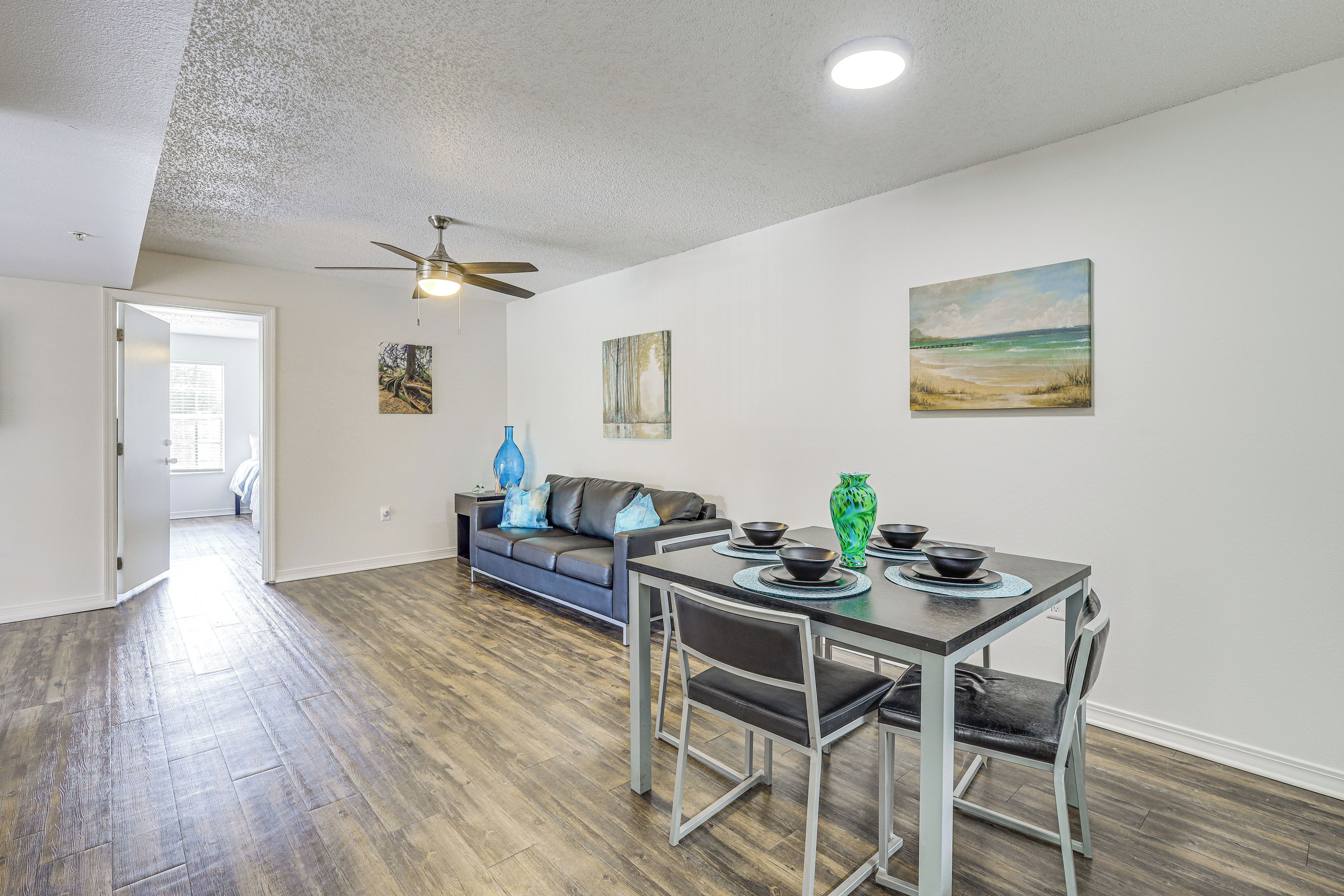 A dining area with a table set for four, a ceiling fan, and artwork on the walls.