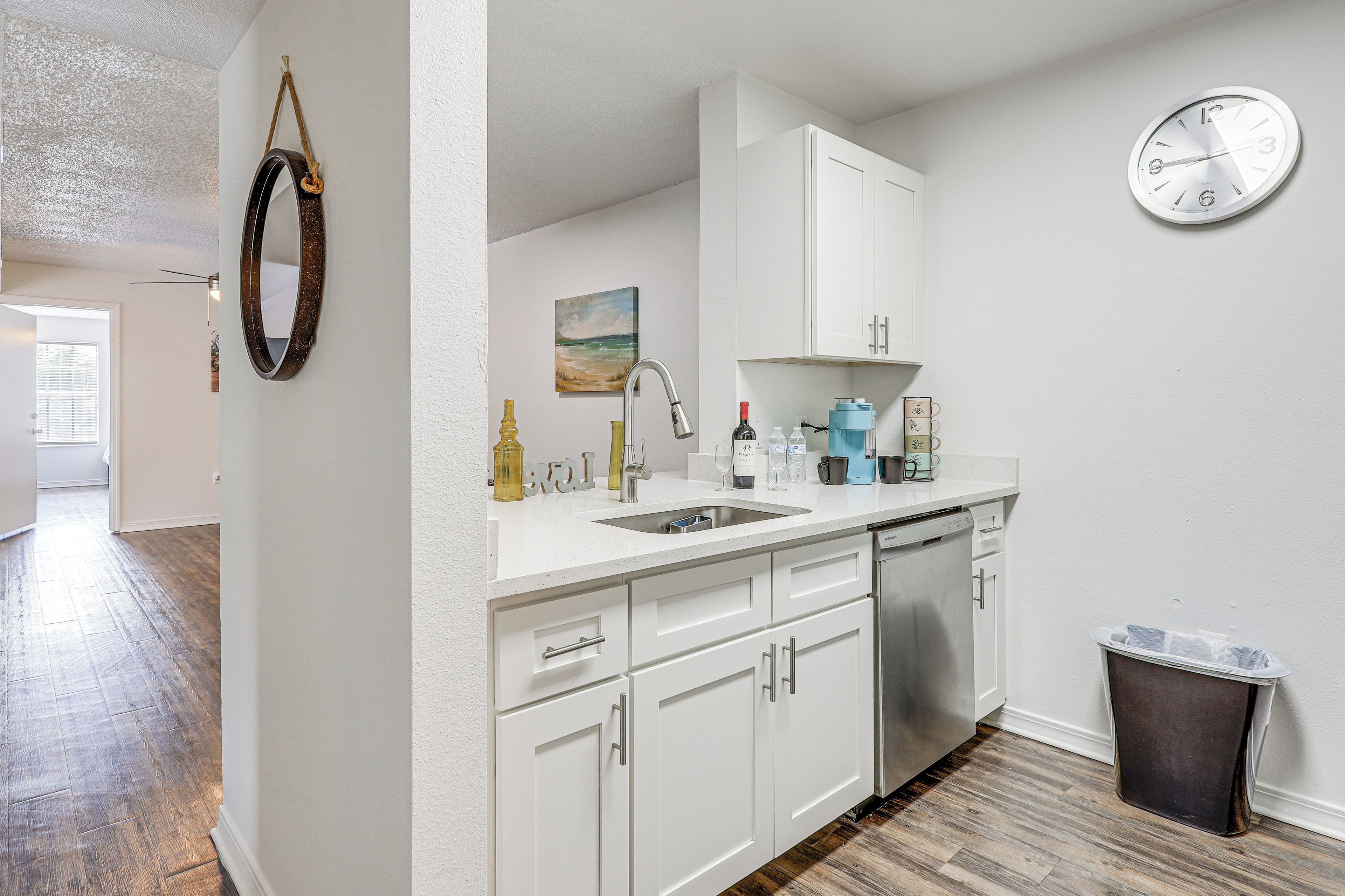 A modern kitchen with white cabinetry, a stainless steel dishwasher, and a wall-mounted clock.