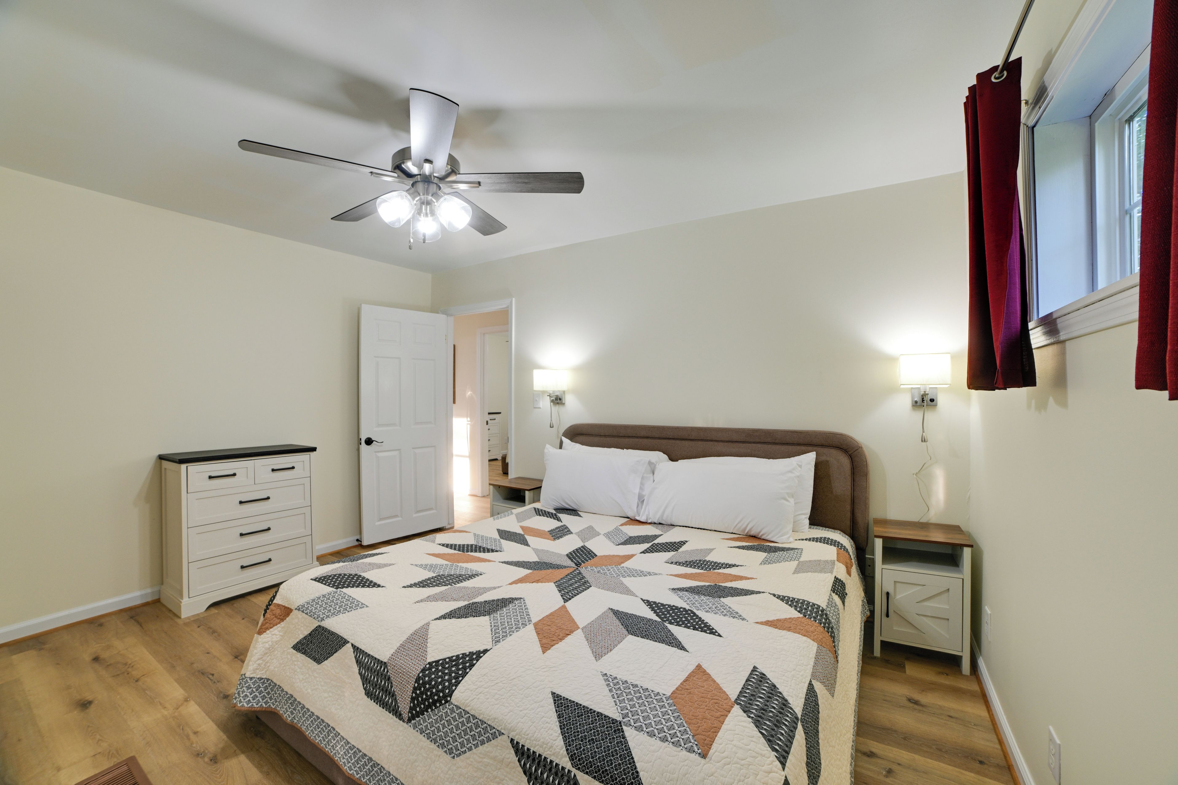 A bedroom with a bed, a nightstand, a dresser, a ceiling fan, and a window with curtains.