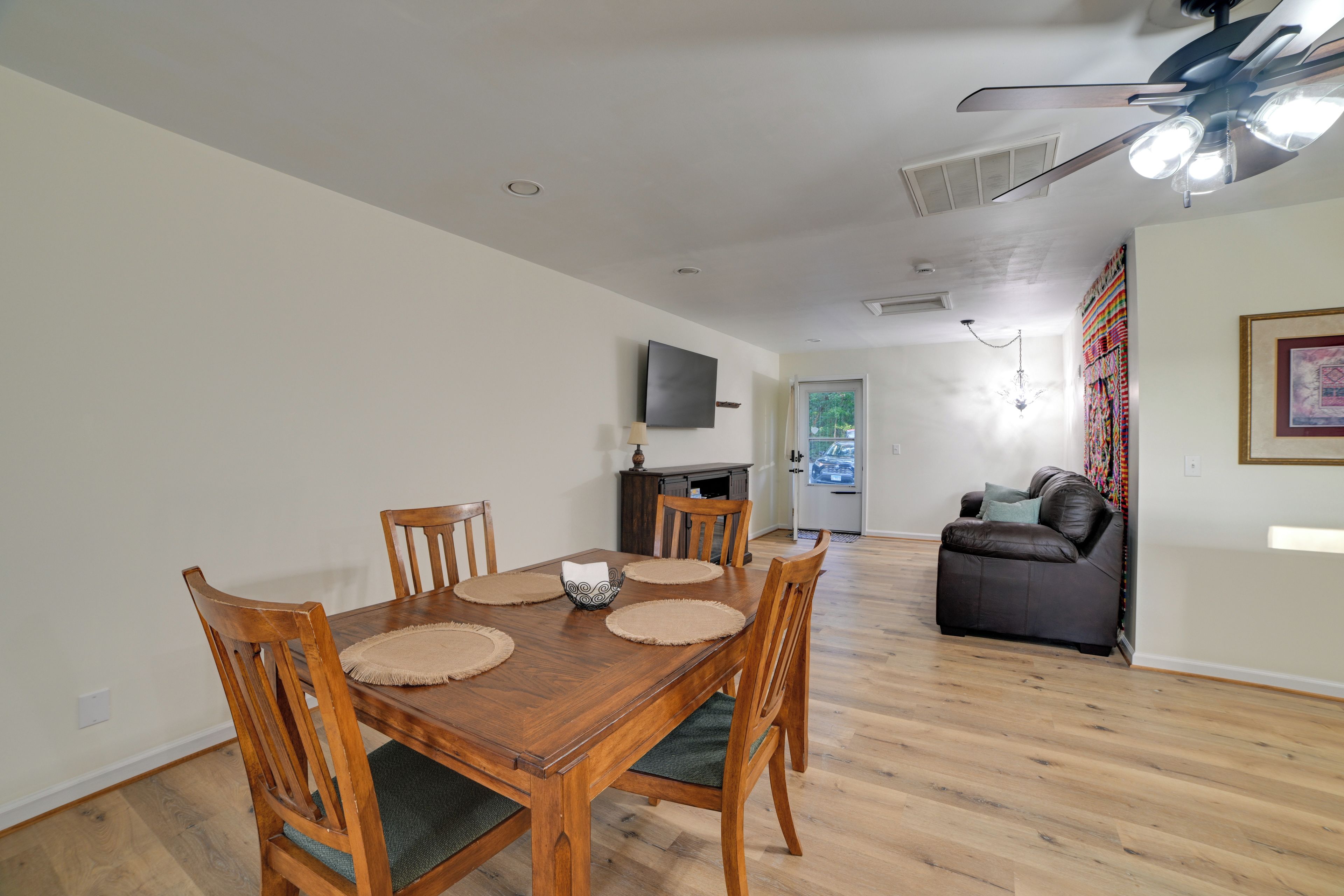 A dining area with a wooden table and chairs, a television mounted on the wall, and a ceiling fan.