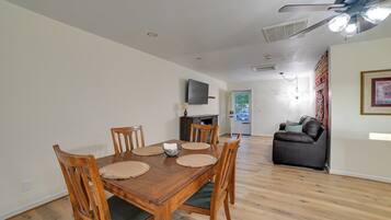A dining area with a wooden table and chairs, a television mounted on the wall, and a ceiling fan.