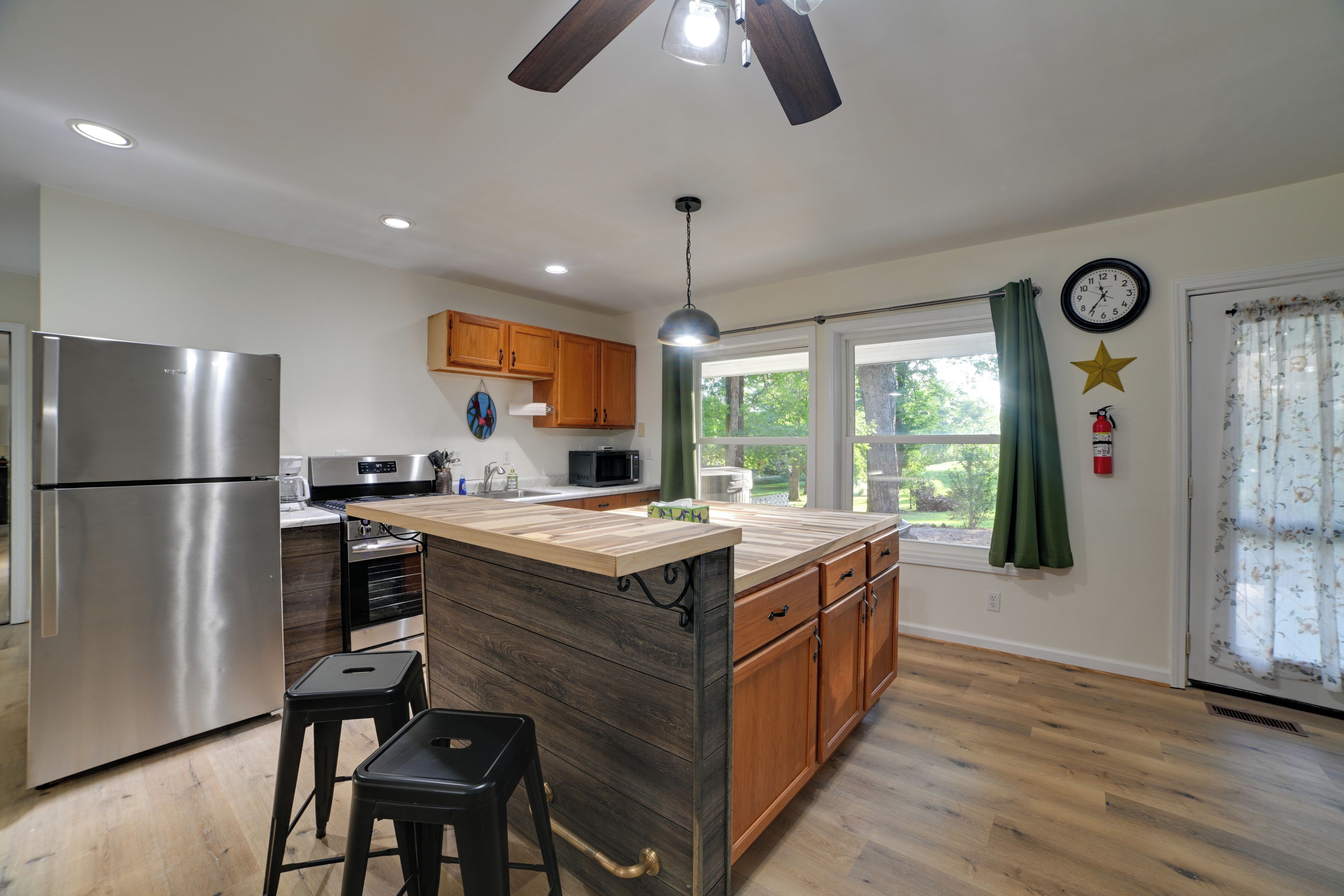 A modern kitchen with a central island, stainless steel appliances, wooden cabinets, and a large window with curtains.