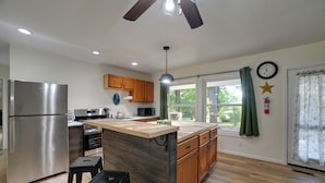 A modern kitchen with a central island, stainless steel appliances, wooden cabinets, and a large window with curtains.