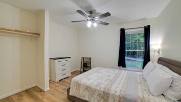 A bedroom with a bed, a ceiling fan, a window with curtains, a bedside table, and a wardrobe.