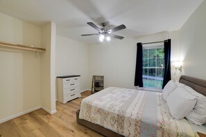 Une chambre à coucher comprenant un lit, un ventilateur de plafond, une fenêtre avec des rideaux, une table de chevet et une armoire.