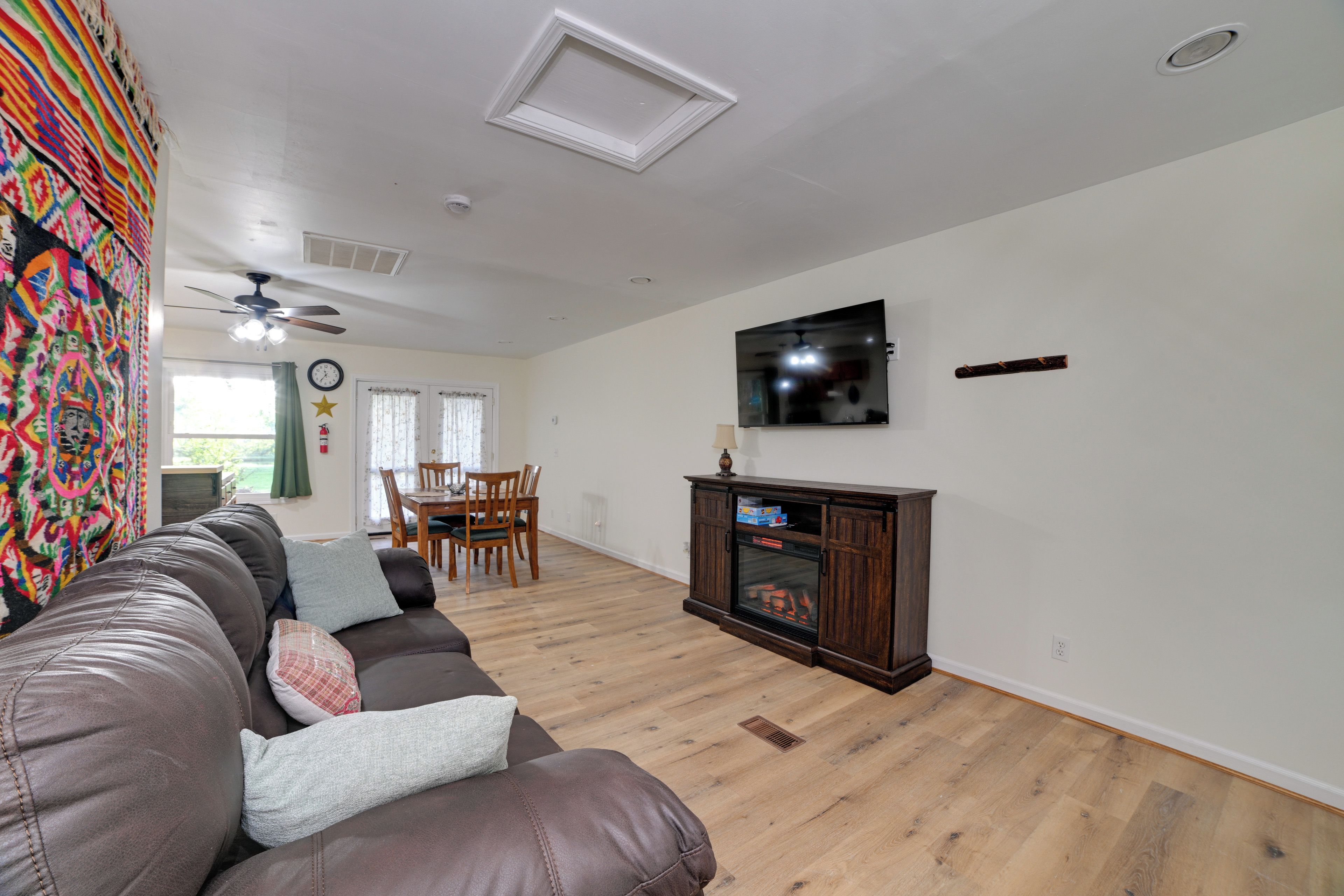 A living room with a brown leather sofa, a flat-screen TV mounted on the wall, a wooden cabinet with a glass door, and a ceiling fan.