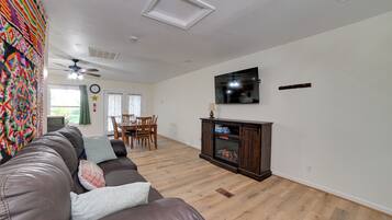 A living room with a brown leather sofa, a flat-screen TV mounted on the wall, a wooden cabinet with a glass door, and a ceiling fan.