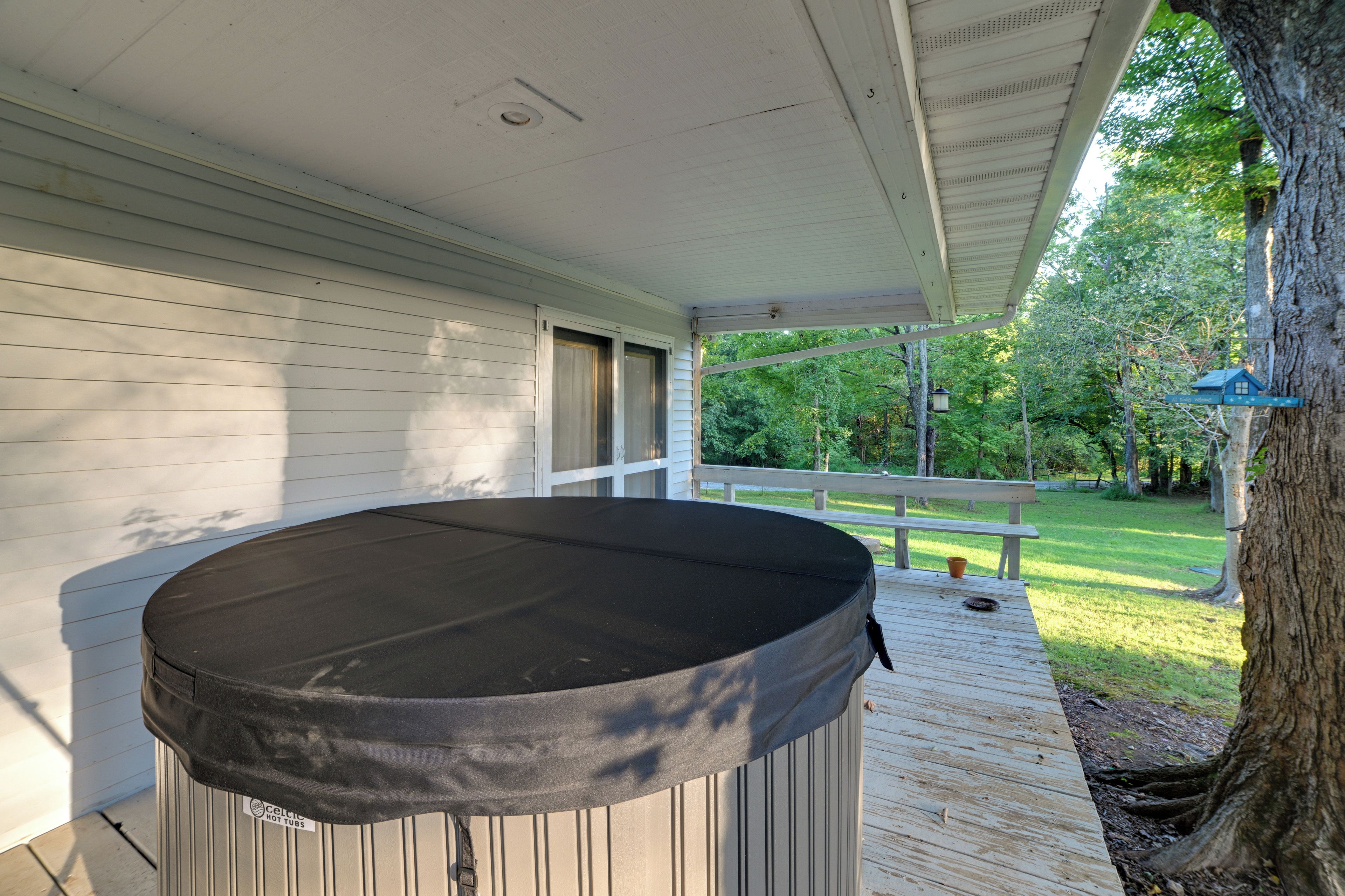 A covered outdoor area with a hot tub, wooden deck, and a view of a garden and trees.