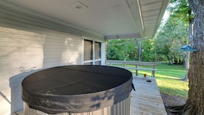 A covered outdoor area with a hot tub, wooden deck, and a view of a garden and trees.