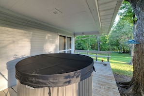 Área externa coberta com hidromassagem, deck de madeira e vista para um jardim e árvores.