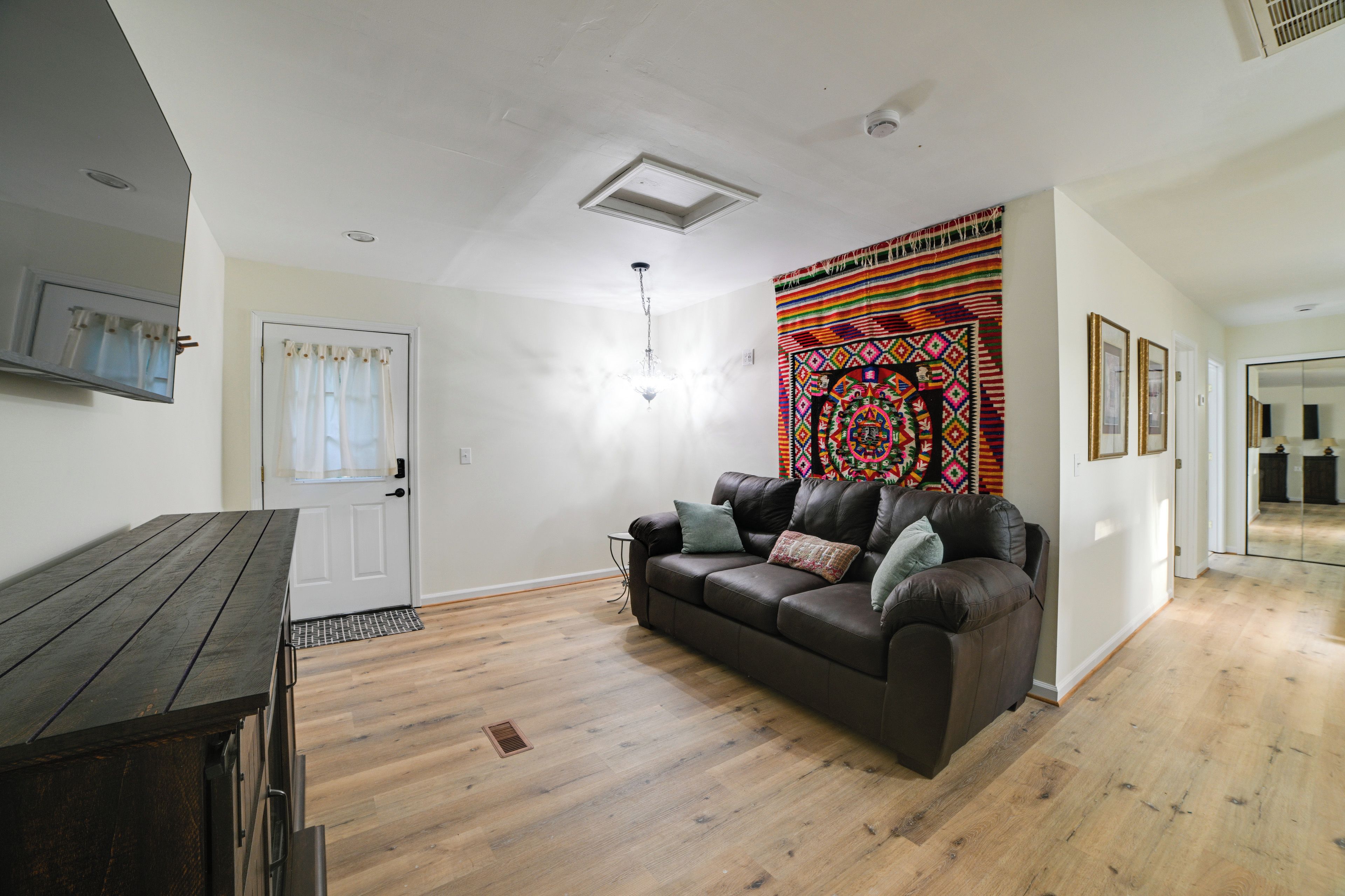 A living room with a brown leather sofa, a wooden coffee table, and a colorful tapestry on the wall.