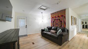 A living room with a brown leather sofa, a wooden coffee table, and a colorful tapestry on the wall.