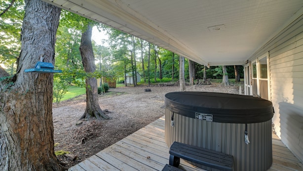 A covered outdoor area with a hot tub, wooden deck, and a tree.
