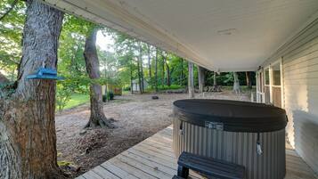 A covered outdoor area with a hot tub, wooden deck, and a tree.