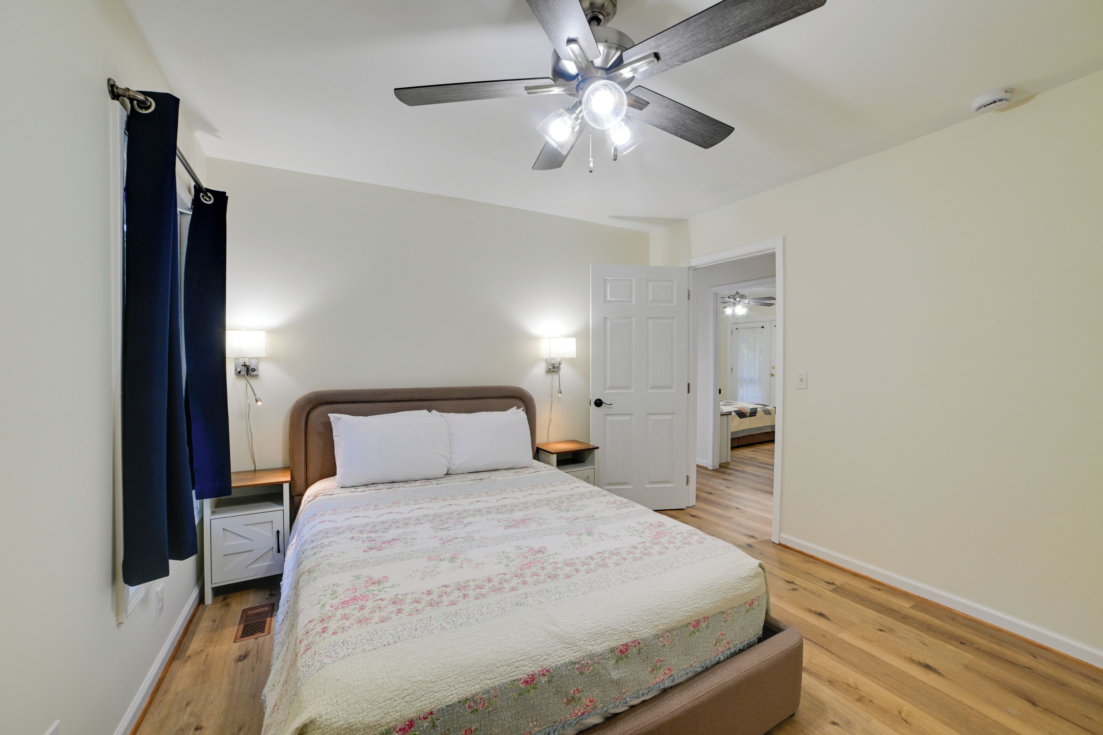 A bedroom with a bed, a ceiling fan, a door, and a nightstand with a lamp.