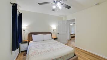 A bedroom with a bed, a ceiling fan, a door, and a nightstand with a lamp.
