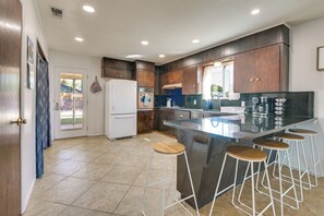 A modern kitchen with a central island, bar stools, a refrigerator, and wooden cabinets.
