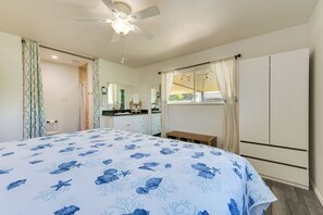 A bedroom with a bed, a ceiling fan, a window with curtains, a bathroom with a shower curtain, and a mirror.