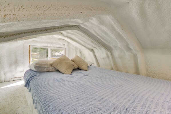 A bedroom with a sloped ceiling, a window, and a bed with pillows.