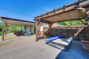 A covered outdoor area with a picnic table and chairs, a wooden fence, and a shaded seating area.