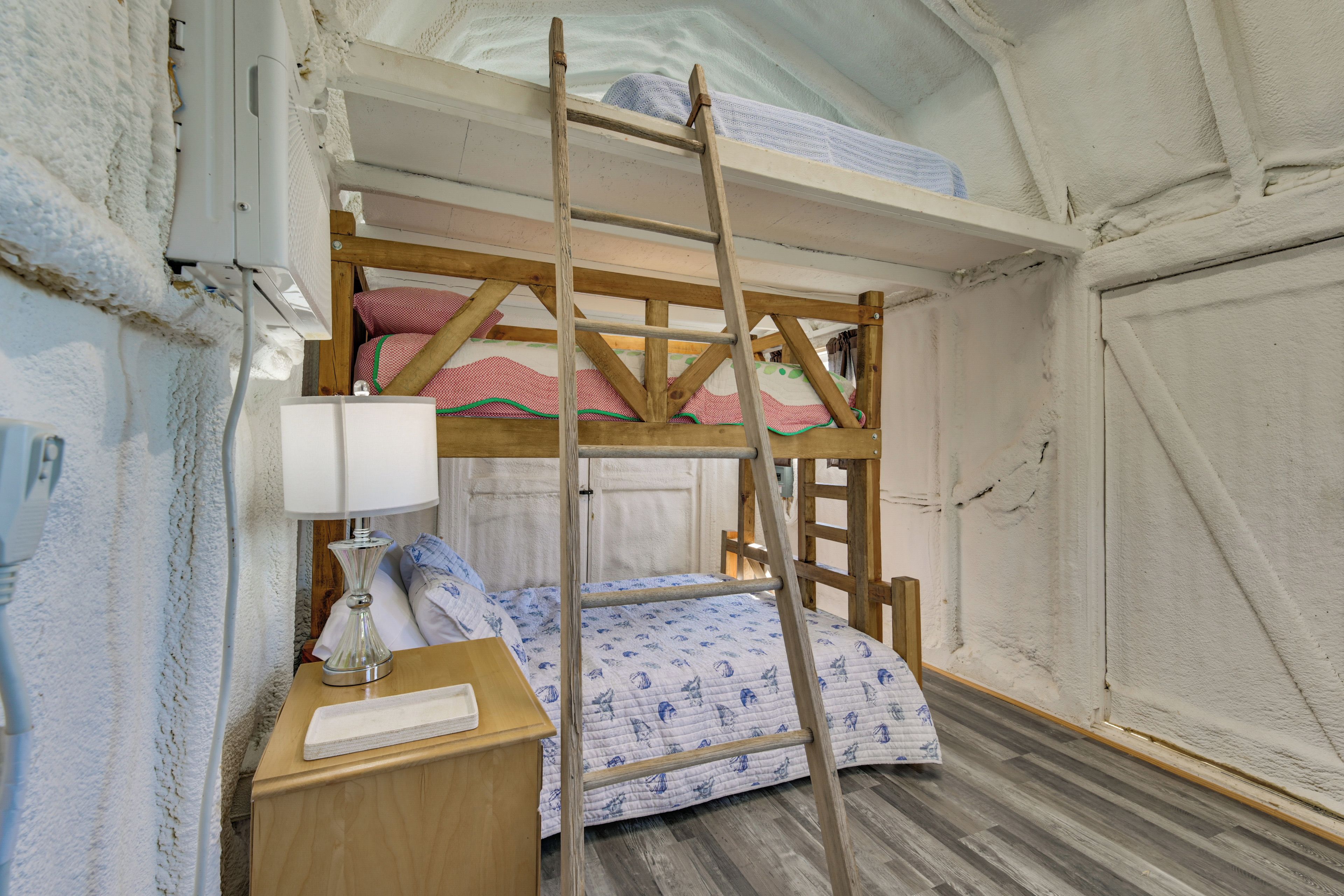 Una cama litera con escalera, una mesita de noche con lámpara y una colcha estampada.
