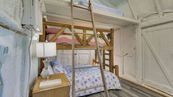Una cama litera con escalera, una mesita de noche con lámpara y una colcha estampada.