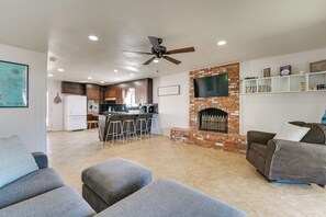 A spacious living area with a fireplace, a kitchen in the background, and a ceiling fan.