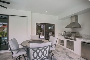 A patio with a round table and chairs, a grill, and a sliding glass door leading to a balcony. - Brand-new Luxury Home w/ Pool! 9 Mi to Pine Island (Cape Coral)